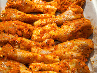 Red hot marinated chicken drumsticks on cooking paper on a old metal cooking tray. Fine poultry product for a large family. Oven cooking.