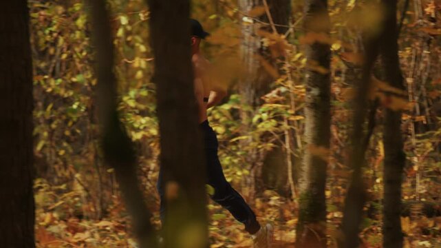 Young muscular man with heart rate monitor on his chest runs along path in an autumn forest on sunny day. Tracking shooting. Concept of sport and benefits of running