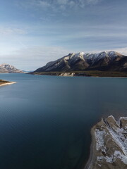 Vertical drone approach toward Abraham Lake&rsquo;s dramatic mountain backdrop &mdash; crystal-clear water, untouched wilderness and alpine winter atmosphere.