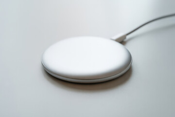 Soft focus close up of a modern, silver and white wireless charging pad on a bright, clean desktop, emphasizing streamlined technology, convenience, and minimalist industrial design.