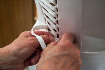 Hands lacing up a white corset on the bride's back. Mother or bridesmaid helping a woman to dress up. Morning wedding preparation detail