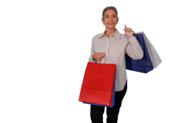 Senior woman shopper carrying colorful shopping bags, smiling and pointing finger up, showing good sales or product. Transparent background