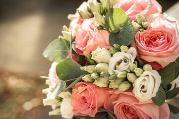 Close-up of two silver wedding rings resting on pink rose petals in a bridal bouquet with white flowers and eucalyptus leaves. Romantic symbol of love and marriage, selective focus