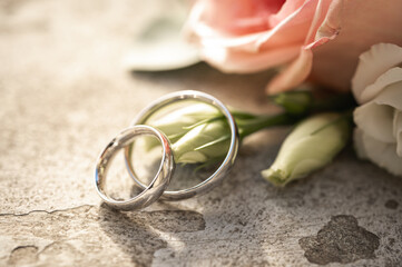 Close-up of two silver wedding rings resting on pink rose petals in a bridal bouquet with white...