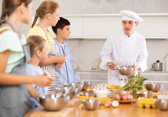 Group of teenagers and friendly chef cook cooking in kitchen. Learn to beat raw eggs