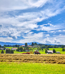 Alter Traktor beim Heu wenden, mit schöner Landschaft und Wolken, in der Nähe von Rottenbuch,...