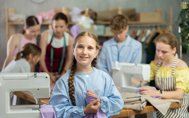 Teenage girl happily shows off a t-shirt he sewed with his own hands on a sewing machine