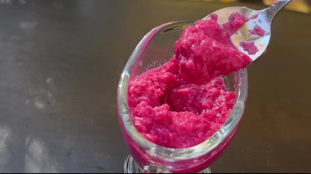 Female hands serve red beetroot horseradish into a yellow plate. Traditional Easter dish preparationsauce glass container on black background spicy