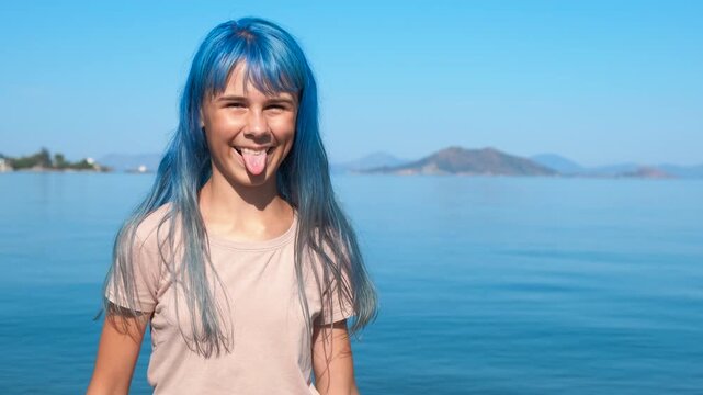 Playful teen show tongue. A playful young girl waving her blue hair and show her tongue on the seashore during summer weekend