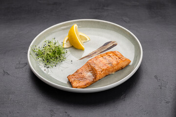 Grilled salmon fillet with lemon and microgreens on plate, gourmet restaurant plating