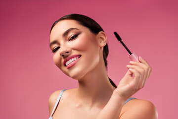 Obraz premium Beautiful Young Woman Modeling with Mascara on Pink Background Highlighting Makeup and Style