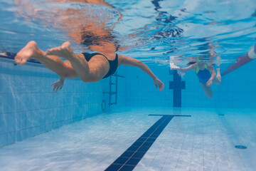 Underwater rear view of two women swimming breaststroke in a blue tiled lane of an indoor sports pool
