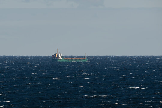 Distant view of green cargo ship sailing on rough dark blue waters of the Baltic Sea horizon