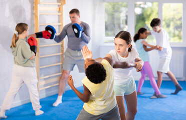 Concentrated tween girl practicing effective self-defense techniques in sparring with boy in training room, using palm to launch blow in chin to rival