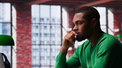 Black man doing remote work feeling uneasy and anxious at desk, shaking his legs and being jittery due to task completion and deadline. Freelancer working under pressure, anxiety. Camera A.