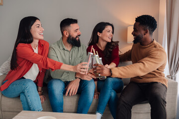 Diverse friends cheering drinks on couch at home