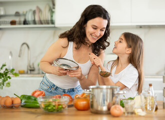 Mom and daughter taste degust soup in kitchen, take out portion of food from pan. Family chefs are pleasantly surprised by result, inhale mouth-watering aroma of food.