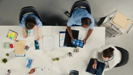 Top down view of surgeons staff in a clinic discussing therapy options and research analysis. The...