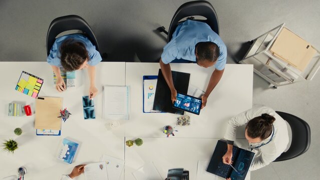 Top down view of surgeons staff in a clinic discussing therapy options and research analysis. The meeting highlights professionalism and innovation in healthcare planning. - Powered by Adobe