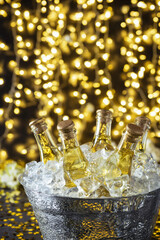Chilled bottles of beverage in a bucket filled with ice, surrounded by a warm, festive bokeh background of golden lights, ideal for celebrations and parties. Christmas and New Year celebration