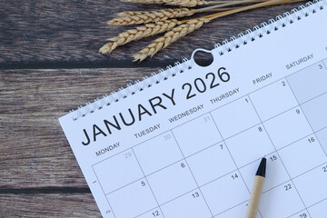 January 2026 new year calendar with pen and wheat bundle on a wooden background. Top view. Annual planning, business goals, weekly organizer concept.
