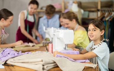 Little enthusiastic girl, about eight, concentrating on sewing in cozy school tailoring workshop,...