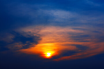 Sky glows with fiery orange and golden hues as sun peeks through scattered clouds, casting dramatic light across the horizon. Deep blue gradient crowns scene, enhancing its vivid contrast