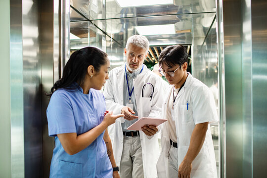 Senior doctor mentoring young medical team on tablet in hospital corridor, focused