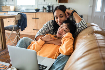 Adult lesbian couple cuddling with laptop at home, affectionate