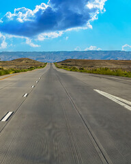 Naklejka premium Open highway through desert hills under bright blue sky 4:5