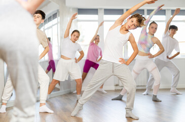 Obraz premium Teenage boy rehearse hip hop dance repeats movements of unrecognizable instructor performance with peers. Preparing for performance of choreographic team, practicing skills, repeating exercises