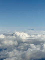 Mountain peak rising above dense cloud layer under clear blue sky from airplane view