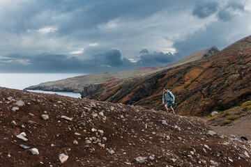 Adventurous hiker navigating rocky terrain along coastal cliffs, surrounded by dramatic clouds and vibrant earth tones, embodying the spirit of exploration and nature's beauty
