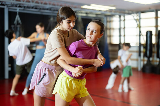 Two teenage girls training self-defense techniques in pairs in studio