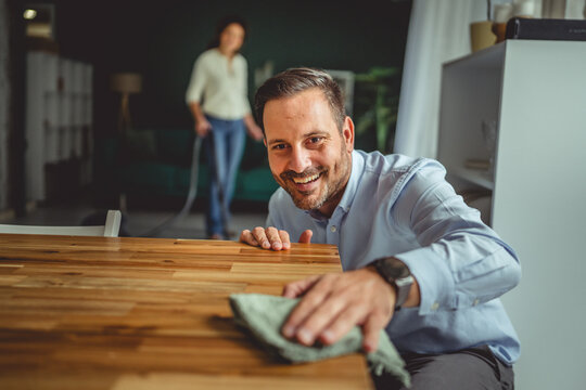 Man cleaning dining table while woman vacuuming in background - Powered by Adobe