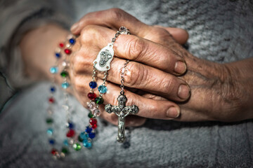 Elderly hands clasped together, adorned with colorful rosary beads, symbolizing faith and family, representing the passage of time and the bond between generations