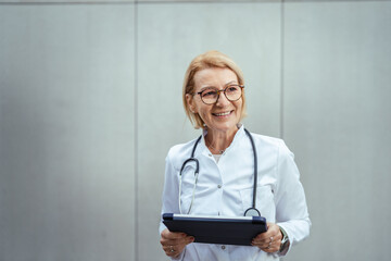 Mature female doctor wearing lab coat holding digital tablet