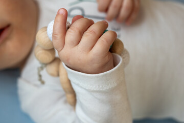 Baby's tiny hand grasping a wooden teething toy, exploring textures and shapes, showcasing early development and growth in a nurturing environment