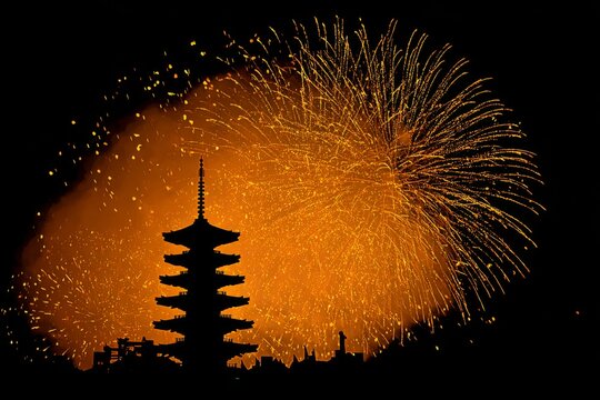 Pagoda silhouette illuminated by radiant gold firework behind it.