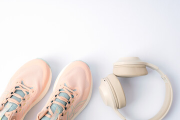 Light pink running sneakers and headphones on white background. Top view, flat lay, copy space