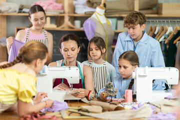 During practical lesson at sewing school, woman teacher shows children example of creating and making dresses.