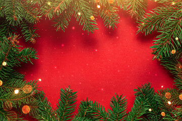 Frame of Christmas tree branches on red background with light and bokeh. Merry Christmas and Happy New Year greeting card. Xmas and Winter holidays. Christmas time, top view