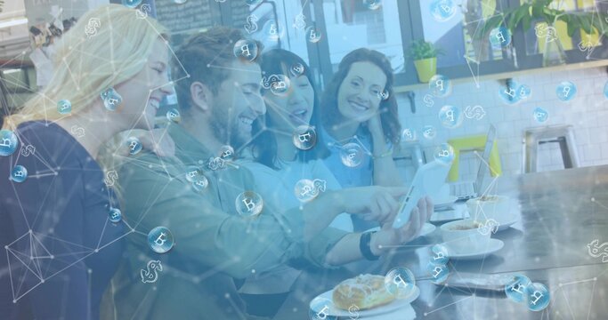 Leaning group of four coworkers in casual clothes checking tablet at cafe table, crypto icons