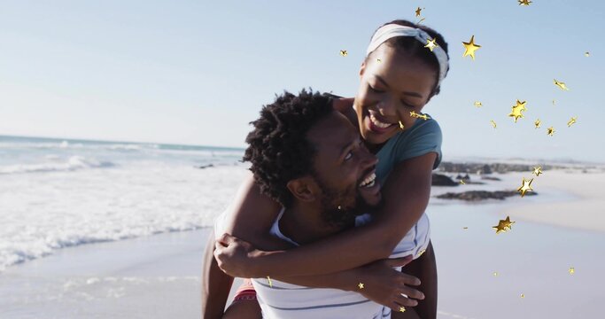 Smiling man in striped shirt piggybacking woman with headband on beach, with gold star overlays - Powered by Adobe