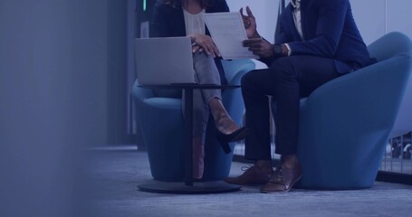 Reviewing colleagues in business attire pointing at documents in office lounge with open laptop