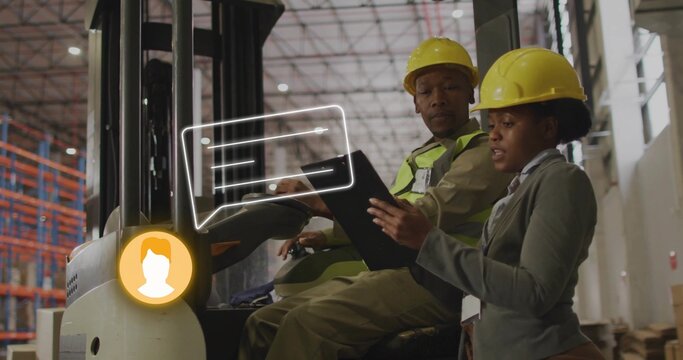Reviewing manager pointing at tablet on forklift in warehouse with yellow hard hats and hi-vis vest