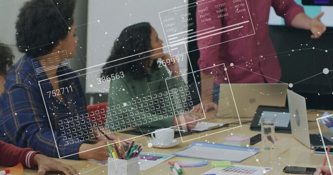Presenting man in maroon shirt gesturing and explaining at meeting table, with laptops, swatches