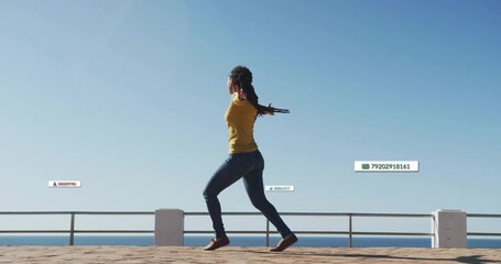Walking woman wearing mustard top and jeans on seaside promenade, metal railing and ocean horizon