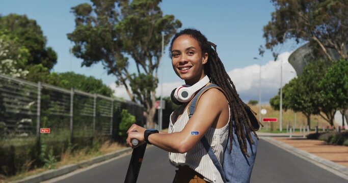 Smiling woman holding electric scooter on campus road, wearing striped top backpack headphones