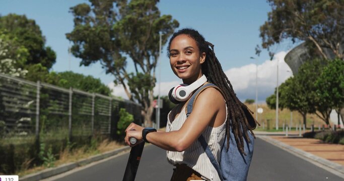 Standing woman holding scooter on suburban road, wearing striped top backpack headphones smartwatch